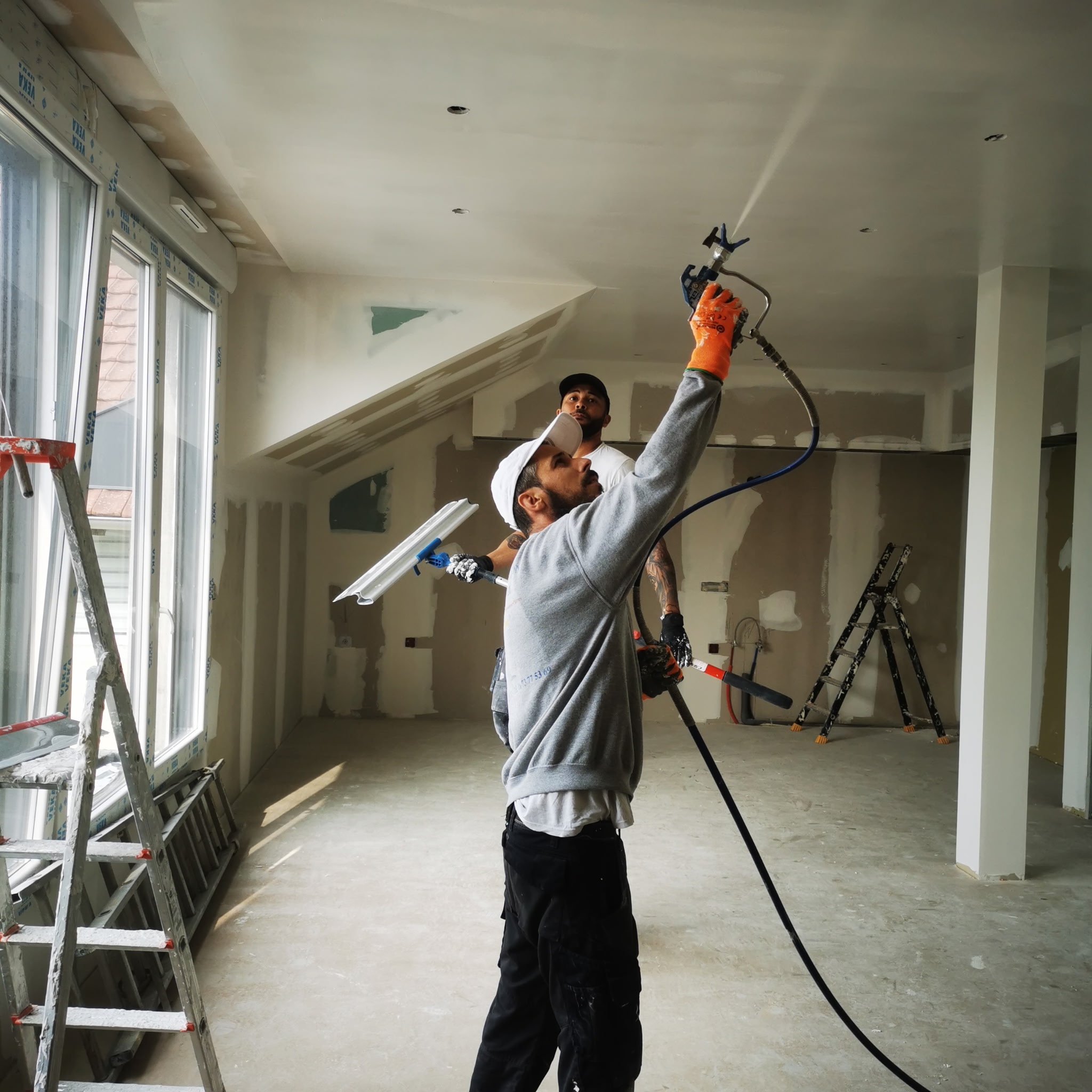 Construction workers wear protective gear while plastering a wall indoors during home renovation.