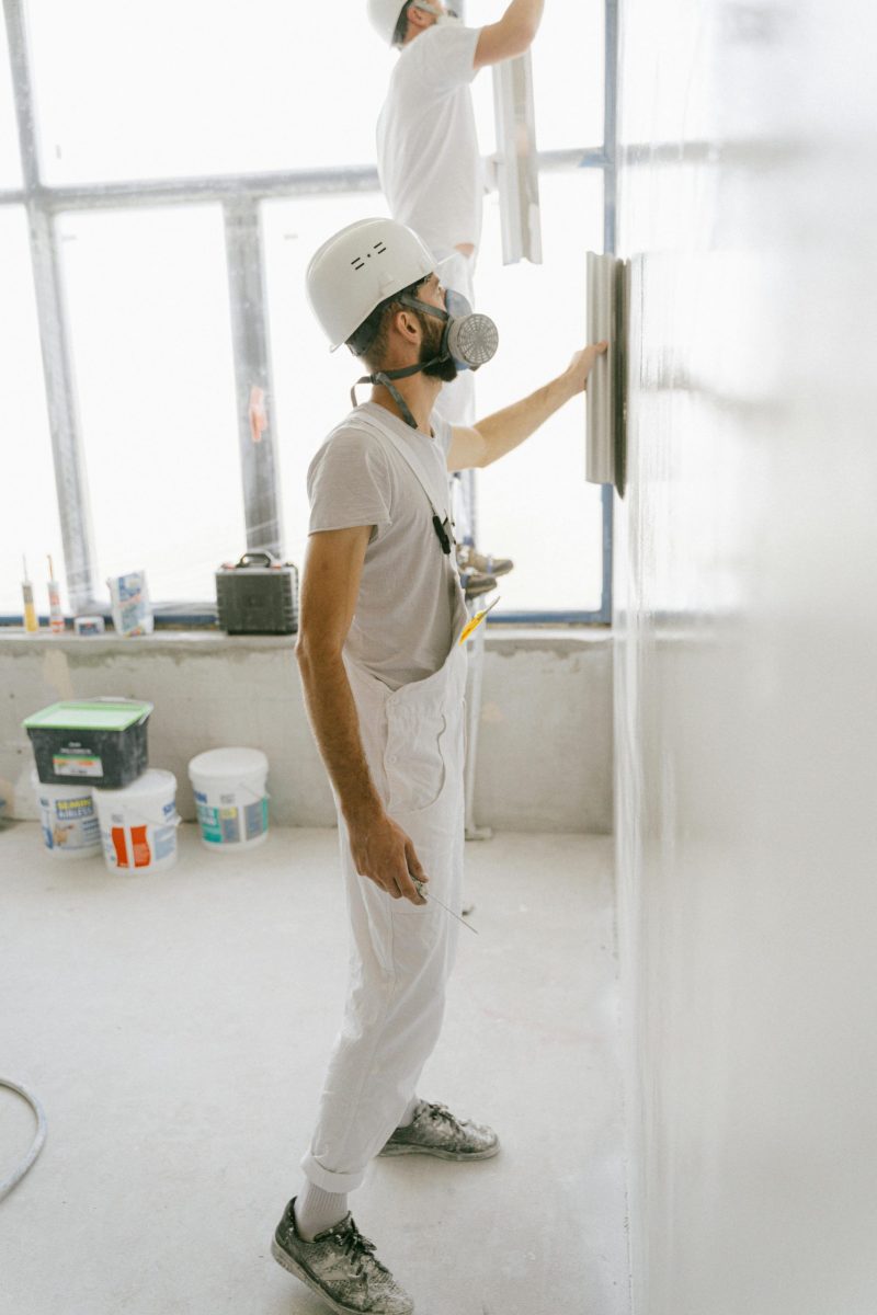 Construction workers wear protective gear while plastering a wall indoors during home renovation.