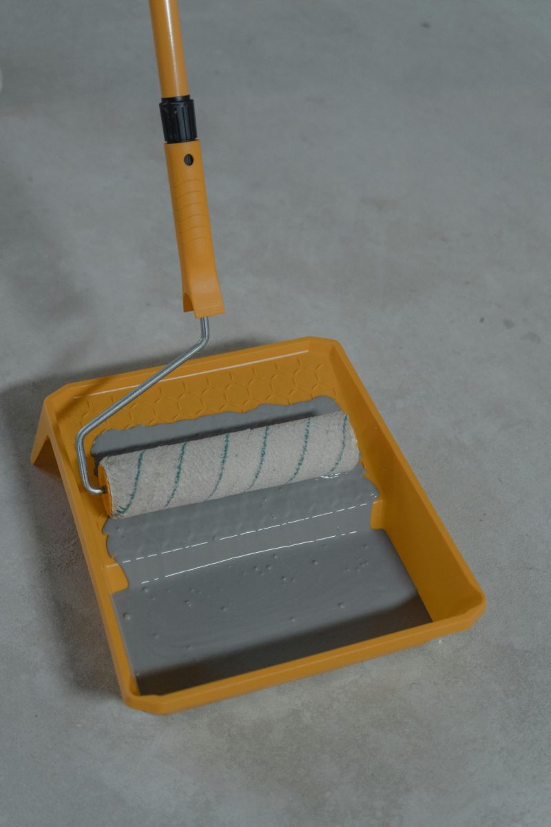 Orange-handled paint roller in a tray filled with gray paint, perfect for DIY projects.